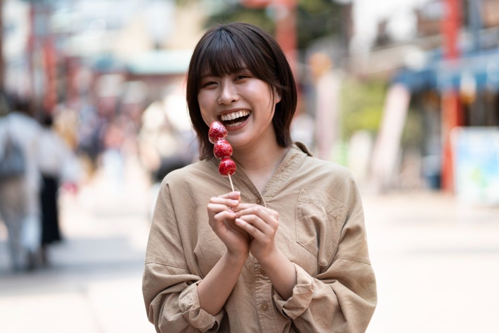 Wanita muda tersenyum lebar sambil memegang jajanan buah stroberi