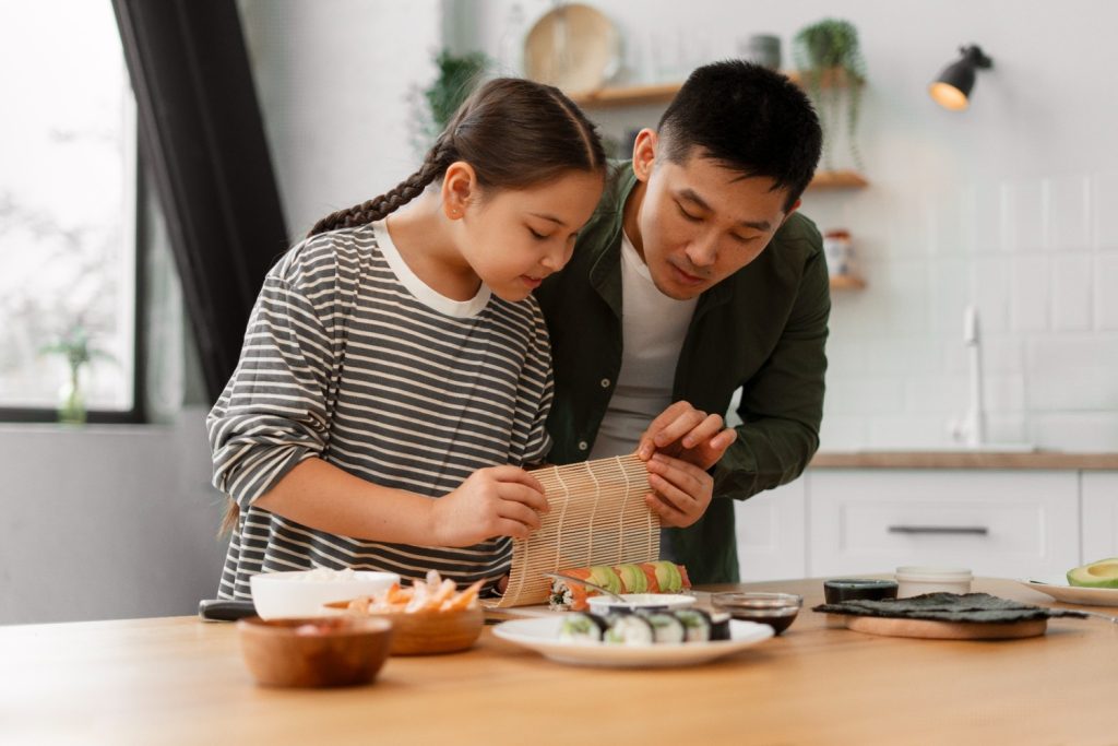 Seorang ayah mengajarkan anak perempuannya cara membuat sushi di dapur.