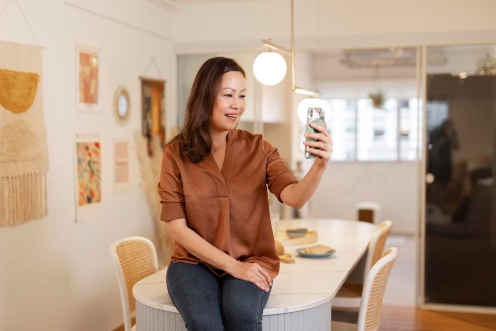 Seorang wanita Asia memegang smartphone sambil duduk di dapur.