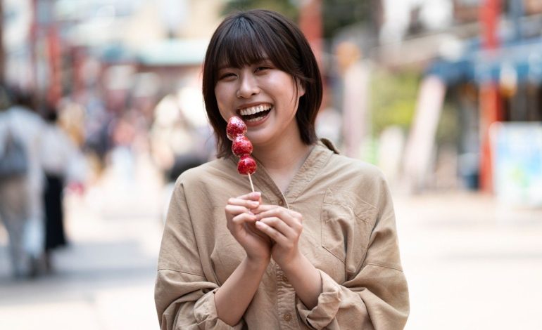 Wanita muda tersenyum lebar sambil memegang jajanan buah stroberi