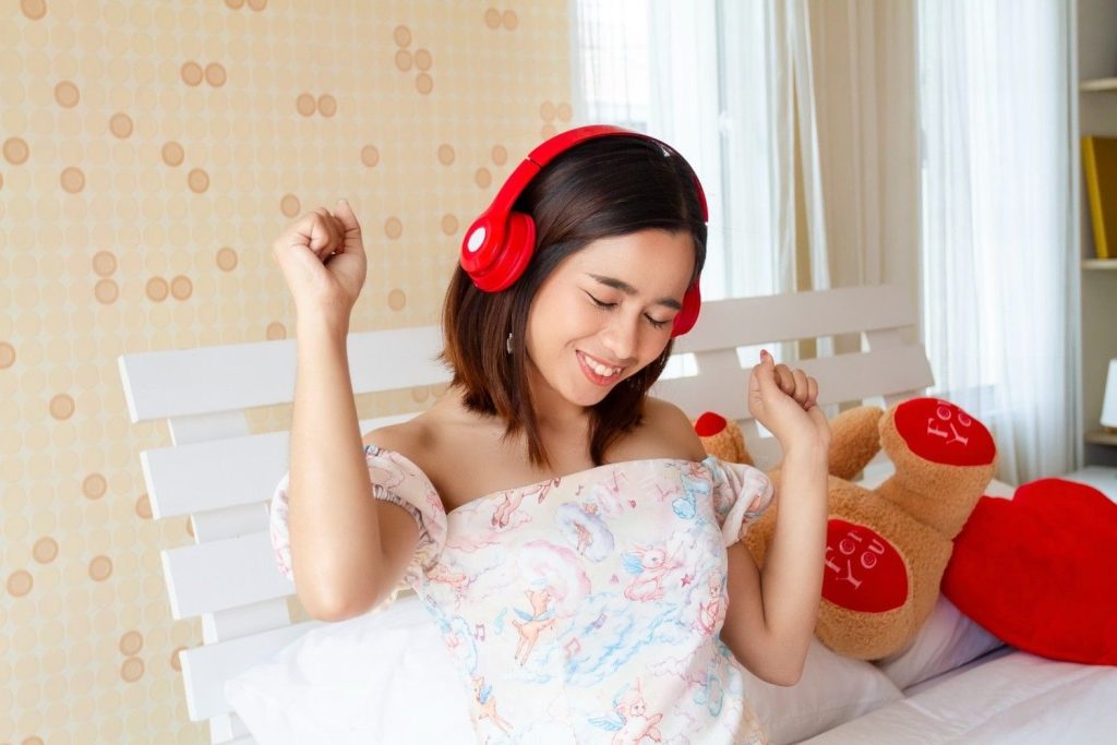 Seorang wanita mendengarkan lagu melalui headphone di kamarnya.