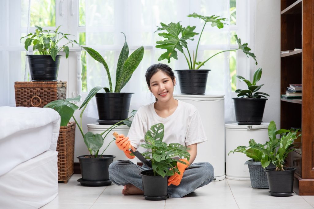 Seorang wanita merawat tanaman di dalam pot yang ada di kamarnya.