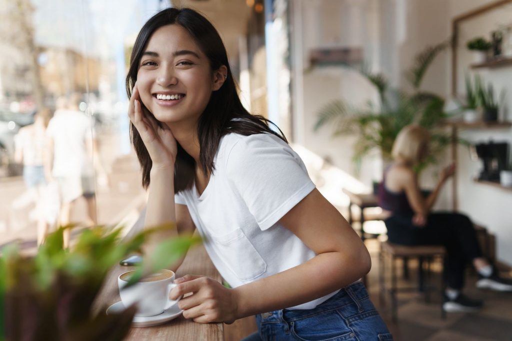 Seorang wanita tersenyum menatap kamera saat menikmati segelas kopi.