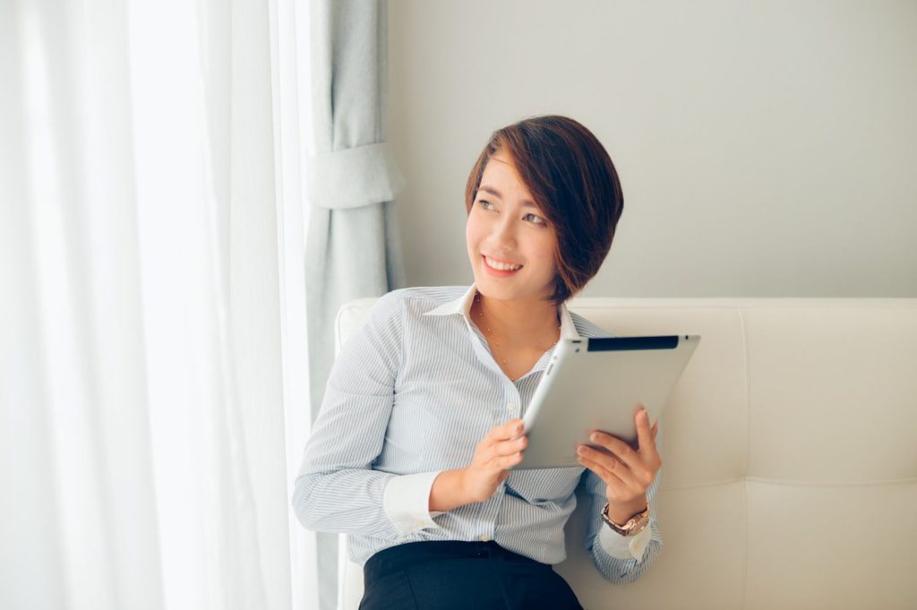 Seorang wanita memegang tablet pintar sambil duduk di sofa.