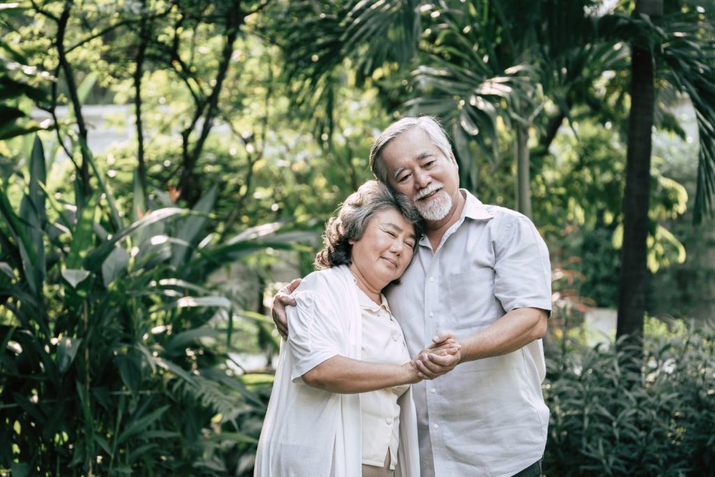 Sepasang kakek dan nenek berpelukan sambil berjalan di taman.