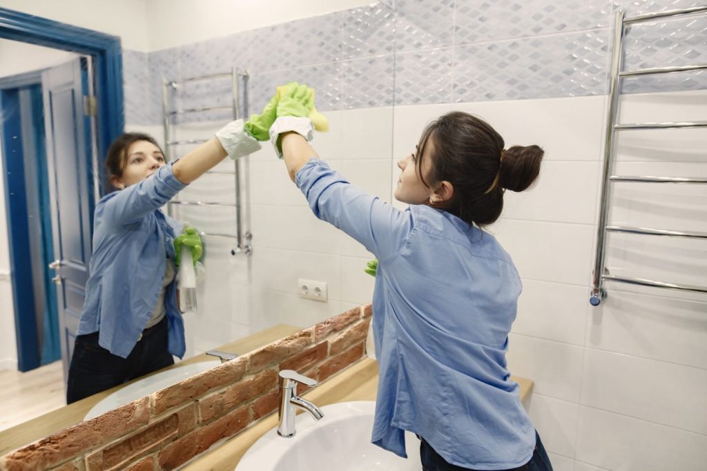 Seorang wanita membersihkan cermin di kamar mandi.