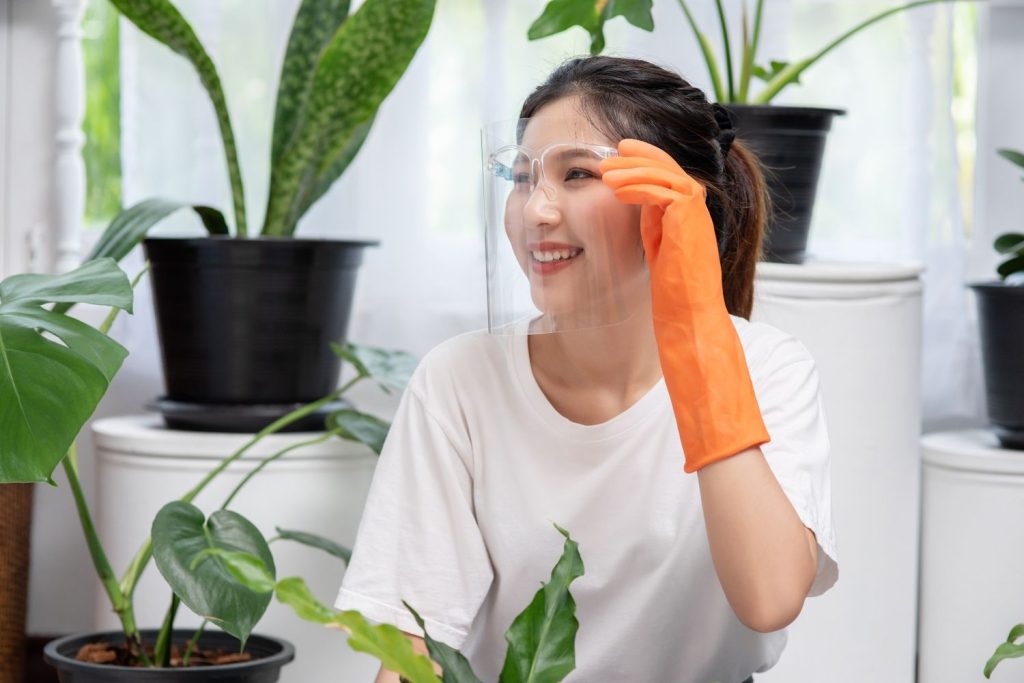Seorang wanita membersihkan rumah sambil mengenakan sarung tangan karet dan face guard.