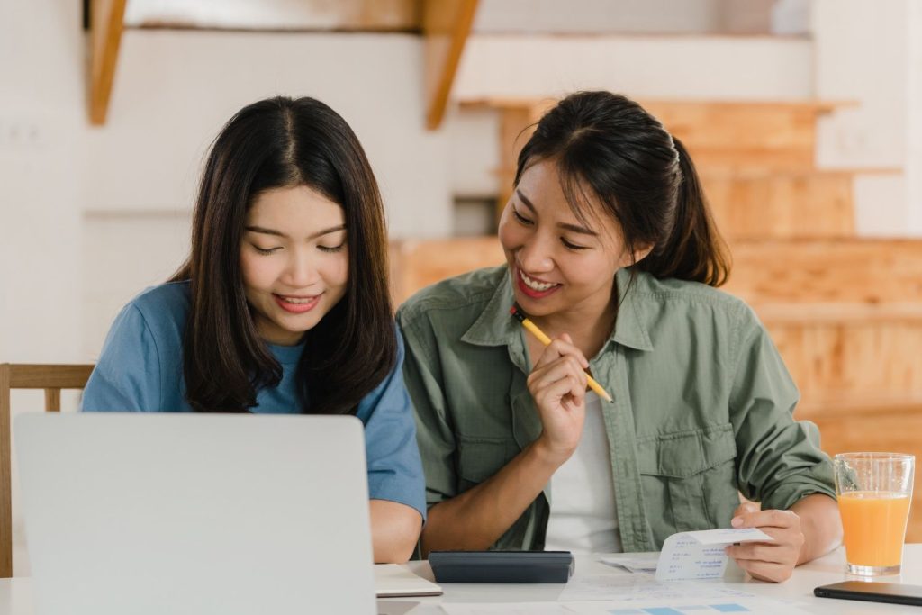 Dua orang wanita sedang belajar cara mengatur keuangan bersama menggunakan laptop.
