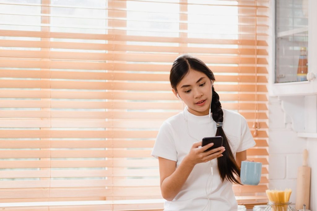 Seorang wanita sedang mendengarkan lagu dari smartphone sambil memegang gelas.