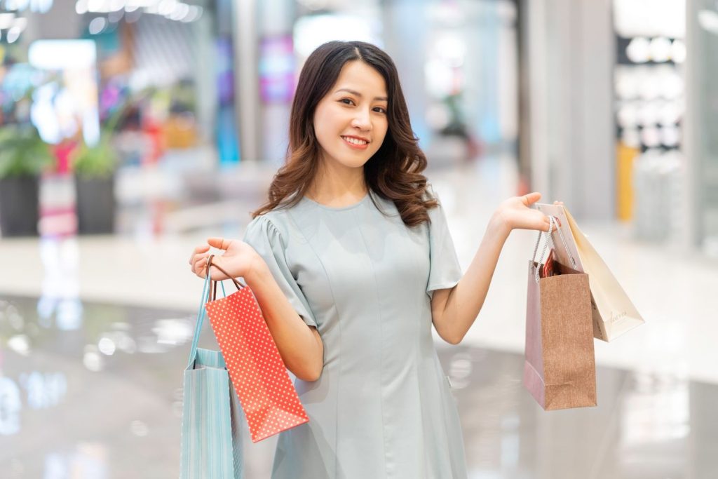 Seorang wanita sedang berbelanja di mall dengan ekepresi bahagia.