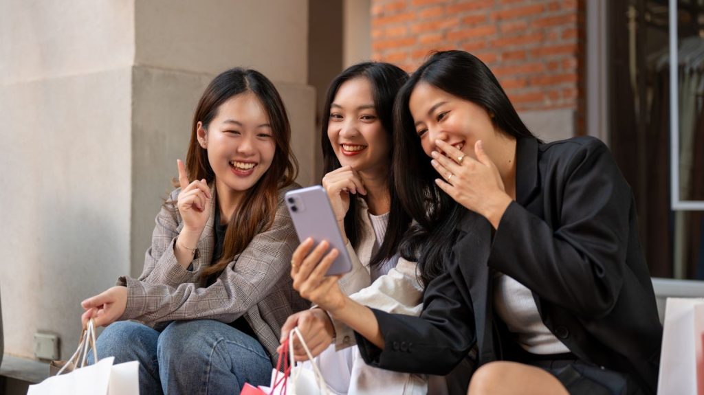 Tiga sahabat wanita sedang tertawa bersama sehabis belanja.