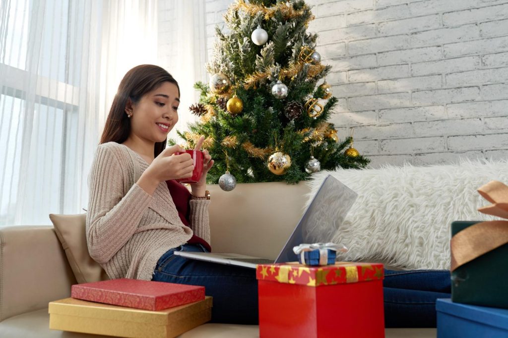Seorang wanita sedang berbelanja online di rumah dengan dekorasi Natal di sekelilingnya.