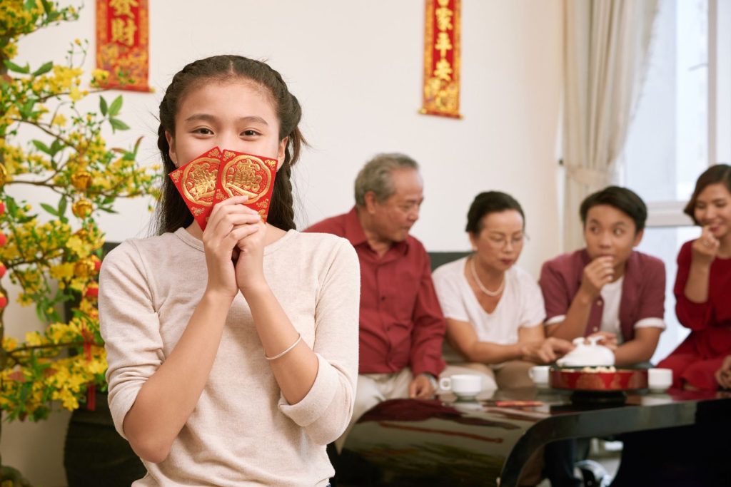 Seorang anak kecil perempuan memegang angpao Imlek dengan wajah gembira.